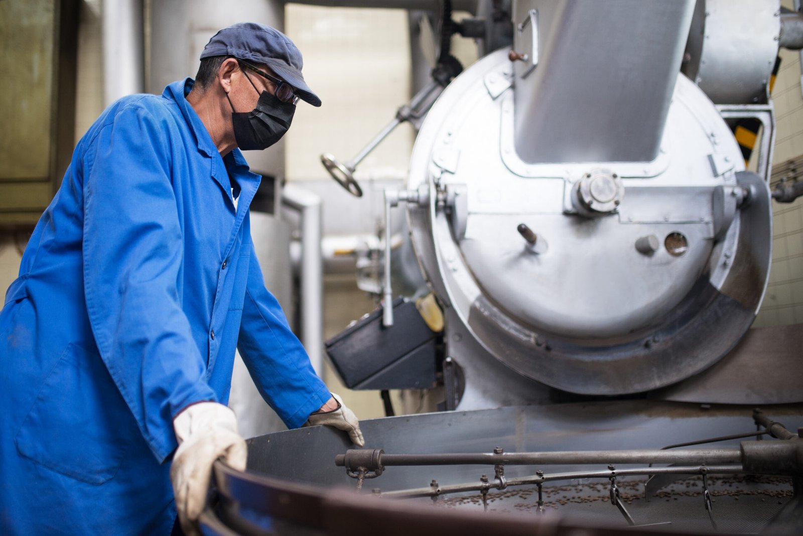 worker in face mask controlling coffee roasting process
